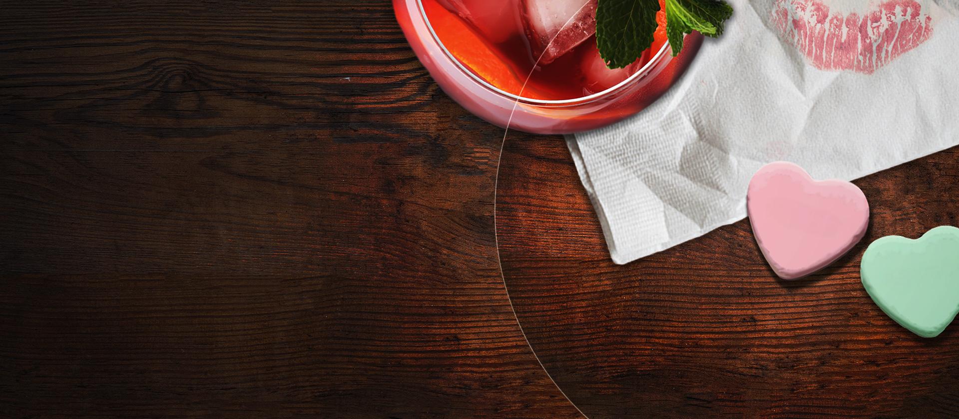 A cocktail is in the left top corner, a napkin with a kiss mark is in the right top corner, 2 conversation hearts are on a table as well as some coins.